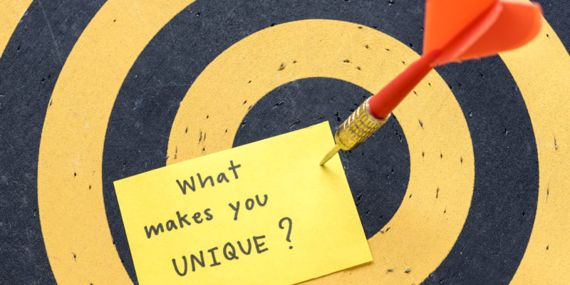 Red arrow hitting yellow note with massage what makes you unique? over dartboard background