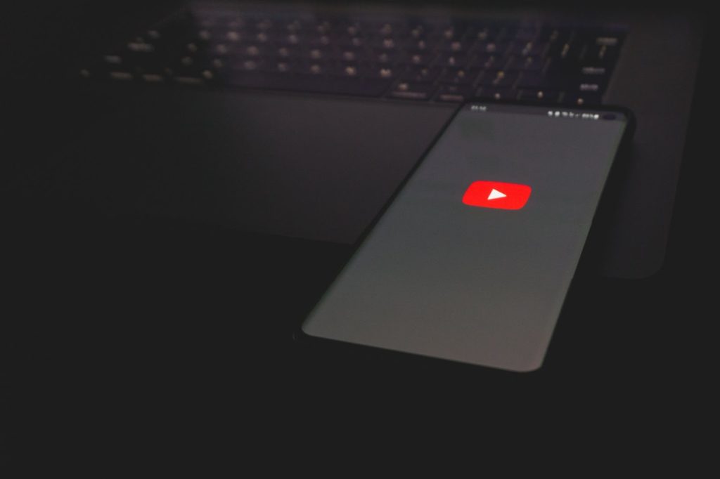Red youtube logo on a black beackground on phone with a laptop in the background